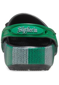 Grüne und graue Clogs mit strukturierter Oberfläche. Enthält einen Riemen mit dem Text "Slytherin" und eine geriffelte Sohle für besseren Halt.