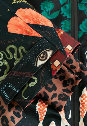 Zbliżenie kolorowej tkaniny z różnorodnymi wzorami, w tym okiem, pomarańczowymi kwiatami, kształtami węża, cętkami lamparta i czerwonymi łuskami ryb.