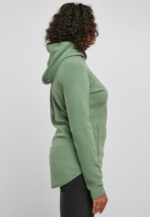 Felpa verde in pile con zip frontale, tasche laterali e cappuccio. Presenta un orlo lungo e curvo e una finitura morbida e texturizzata.