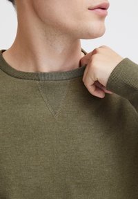 Pulover verde măsliniu cu guler ribot și detalii de cusătură la guler. Textură moale, design ajustat și mâneci lungi.