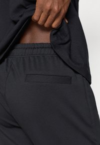 Czarne szorty wykonane z gładkiego materiału, z elastyczną talią i małą kieszonką na tyle do przechowywania.