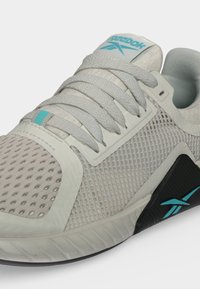 Λευκό και ανοιχτό γκρι παπούτσι Reebok με τυρκουάζ λογότυπο στη γλώσσα και στη μεσαία σόλα, υφασμάτινη υφή στο επάνω μέρος και γκρι κορδόνια δεμένα προσεκτικά.
