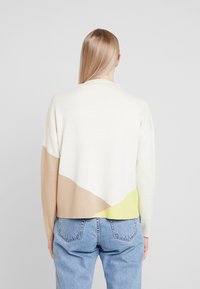 Suéter de punto en beige, blanco y amarillo con un patrón geométrico. Corte relajado, escote redondo y textura suave.