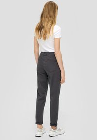 Pantaloni grigi a vita alta con risvolti, due tasche posteriori e una texture liscia, abbinati a sneakers bianche e una T-shirt bianca aderente.