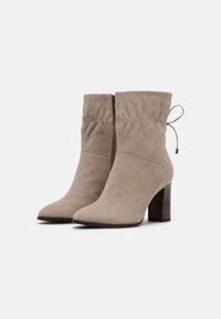 Bottes chelsea beige en suède avec un bout effilé, fermeture éclair et détail de tige froncée. Présente un talon en bois.