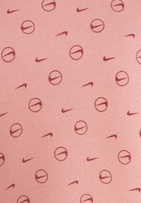 Ljusrosa tyg med ett genomgående mönster av röda Nike-swooshar och cirkulära logotyper, vilket skapar en upprepad design över materialet.