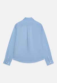 Ljusblå långärmad skjorta med knappar sedd bakifrån, med en centrerad veck och knappade ärmslut på vit bakgrund.