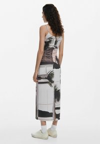Abito midi senza maniche in morbido tessuto setoso che presenta un motivo geometrico e motivi tropicali. Ha uno spacco laterale e una silhouette aderente.