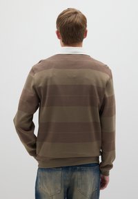 Brauner gestreifter Pullover mit weißem Kragen, aus einem Strickstoff gefertigt. Die Streifen wechseln in Brauntönen, mit langen Ärmeln und einer lockeren Passform.