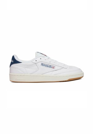 Hvid lav Reebok sneaker med marineblå hældetalje, gummisål og logo med Union Jack på siden og tungen mod en hvid baggrund.