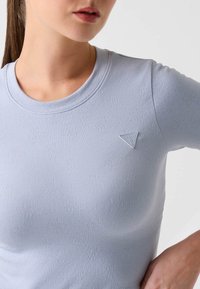 Hellblaues, geripptes T-Shirt mit rundem Ausschnitt und einem kleinen dreieckigen Logoaufnäher auf der linken Brust. Weiche, dehnbare Stoffstruktur.
