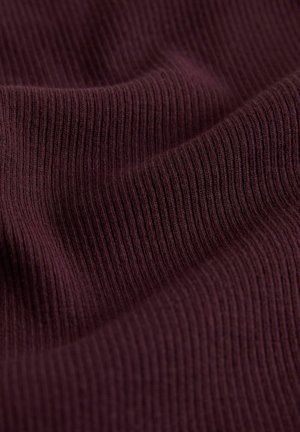 Tuvplāns ar tumši violetu riboto audumu, redzama tekstūra un mīkstas krokas, kas veido vieglas viļņveida līnijas.