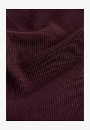 Tuvplāns ar tumši violetu riboto audumu, redzama tekstūra un mīkstas krokas, kas veido vieglas viļņveida līnijas.