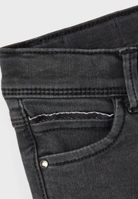 Pantalones vaqueros negros de mezclilla con detalles de tachuelas metálicas, que cuentan con un pequeño bolsillo frontal con una costura blanca en contraste y una textura suave.