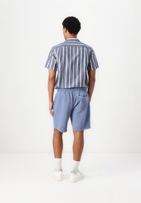 Kortærmet skjorte med lodrette blå og hvide striber, parret med blå shorts og hvide sneakers. Enkel design med en afslappet pasform.