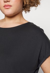 Czarny top z krótkim rękawem o szerokim dekolcie i miękkiej teksturze. Materiał wydaje się lekki i codzienny, z minimalnymi detalami szycia.