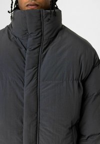 Pufferjack in donkergrijs, met een hoge kraag, een geborduurde textuur en een lichtgewicht ontwerp met zichtbare stiksels.