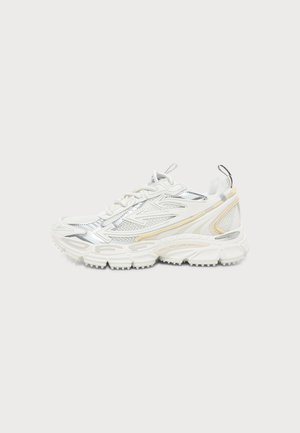 Weißer und silberner Sportschuh mit Mesh-Elementen, strukturierter Sohle und gelben Akzenten, seitlich auf einfachem Hintergrund dargestellt.