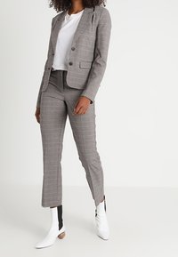 Grå rutigt kostym med en figursydd kavaj och skräddarsydda byxor, kombinerad med en vit skjorta och vita ankelboots med svarta accenter.