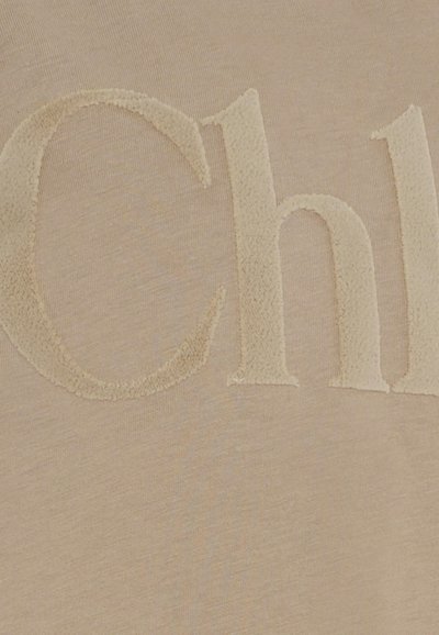 Beżowa bluza z wyraźnym, teksturowanym, welurowym wytłoczonym napisem w nieco jaśniejszym odcieniu beżu.