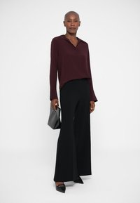 Burgundy színű, hosszú ujjú blúz gallérral, fekete, bő szárú nadrággal párosítva. A modellen egy fekete clutch található, amit hegyes orrú fekete cipők egészítenek ki.