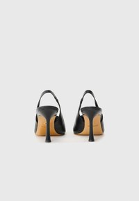 Escarpins slingback en cuir noir avec un bout pointu et un talon aiguille effilé. Texture lisse avec un design minimaliste et une marque discrète.