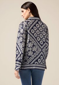 Blusa a fantasia navale con design floreali e accenti geometrici. Maniche lunghe con polsini abbottonati, colletto e taglio dritto.