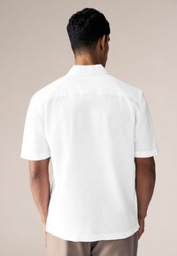 Bijela košulja kratkih rukava od laganog materijala, s klasičnim ovratnikom, ravnim rubom i minimalnim detaljima šavova.