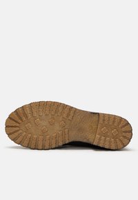 Suela de una bota marrón con un patrón de diseño grueso y resistente, diseñado para proporcionar agarre, vista desde abajo contra un fondo blanco liso.