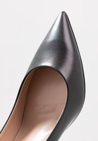 Scarpa nera in pelle con tacco alto, punta affusolata e finitura liscia e lucida; presenta un design a ritaglio sui lati.