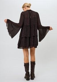 Vestido de leopardo de color marrón oscuro con tres niveles, tela transparente y mangas acampanadas. Abotonado en el cuello con un detalle de ojal en la parte posterior.