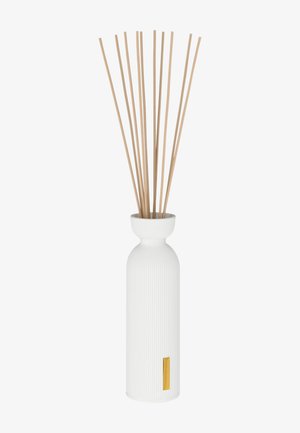 Diffuseur de parfum en céramique blanc à nervures, avec un col arrondi et des tiges en bambou. Présente une étiquette dorée en accent à la base.