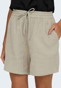 Beige lightweight shorts with an elastic waistband and adjustable tie, featuring pockets and a textured fabric with a grid pattern.