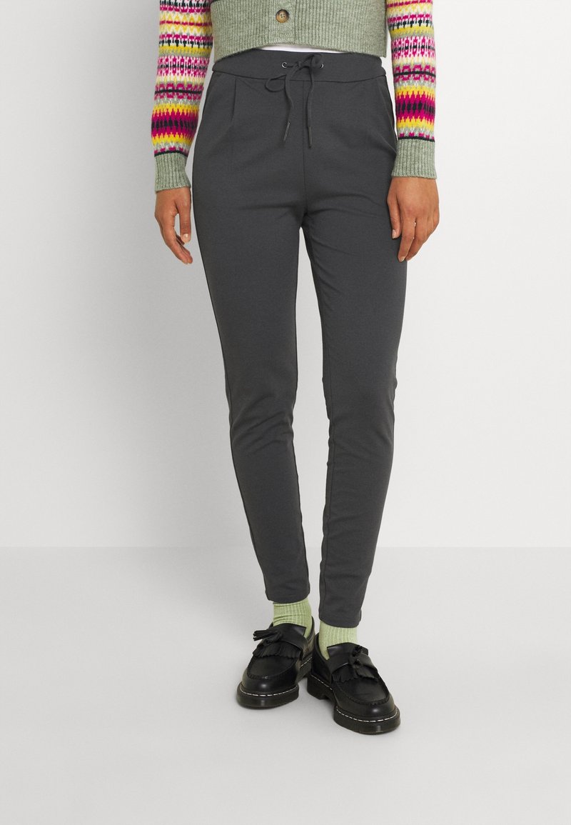 Personne portant un pantalon gris foncé à cordon, des chaussettes vertes, des mocassins noirs et un cardigan vert avec des manches rayées colorées.