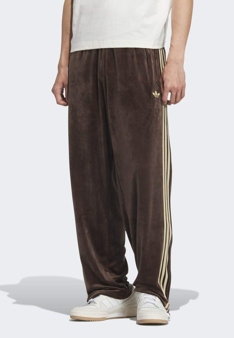 Bruine velours joggingsbroeken met gouden zijstrepen en kleine logodetails. Losse pasvorm met een zachte textuur, gecombineerd met witte sneakers.