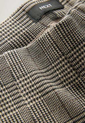 Närbild av svart och beige houndstooth-mönstrad tyg med synlig Next-märke sydd på en klädesplaggskrage.