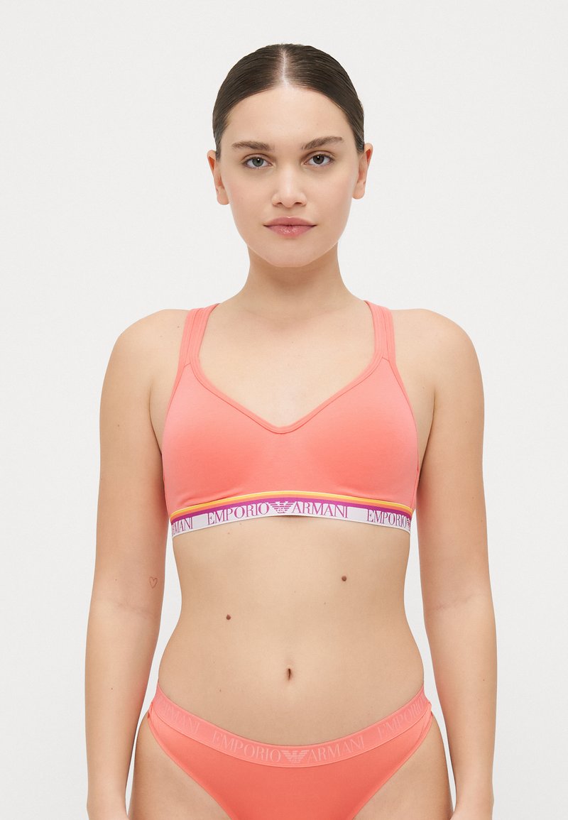 Coral sports bra with a v-neck design, adjustable straps, and an elastic band featuring "Emporio Armani" in purple and yellow accents.