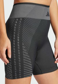 Pantaloni sportivi neri con vita alta, tessuto testurizzato e strisce diagonali grigie, con cuciture rinforzate e un branding sottile.