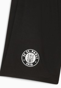 Melnas audums ar baltu apaļu FC St. Pauli 1910 logotipu, kuram attēlota vēsturiska ēka ar krustu un zvaigznēm.