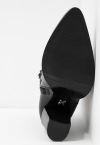 Botte en cuir noir avec bout pointu, talon empilé, zip sur le côté, et "BRONX" embossé sur la semelle faisant face à l'objectif.