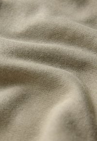 Béžová bavlnená tkanina s jemnou textúrou, s subtílnym tkaným vzorom a hladkou padavosťou, ukazujúca jemné záhyby a vrásky.