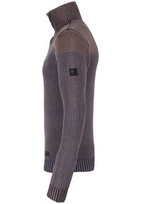 Sidosyn av en långärmad, texturerad stickad tröja med hög ribbad krage i två nyanser av brunt och grått.