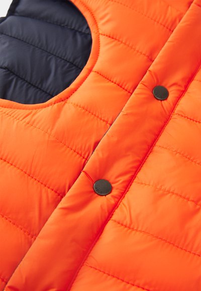 Gros plan d'un gilet matelassé orange avec des boutons-pression noirs et une doublure intérieure bleu marine visible près du col.
