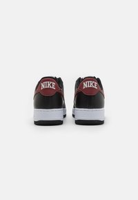 Baskets Nike noires et bourgognes avec des accents blancs. Matériau en cuir lisse, bout rond, semelle en caoutchouc et logo au talon.