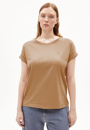 Braunes kurzärmliges T-Shirt mit Rundhalsausschnitt, aus weichem Material gefertigt. Mit umgeschlagenen Ärmeln und kleinem Logo auf der Brust. Kombiniert mit blauen Jeans.