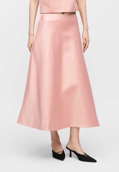 Γυναίκα που φοράει ροζ σατέν φούστα με ψηλή μέση και μήκος μέχρι τον αστράγαλο, συνδυασμένη με μαύρες ψηλοτάκουνες mule με μυτερή μύτη.