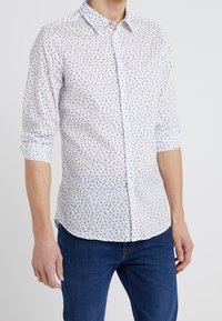 Camicia a bottoni bianca con un piccolo motivo floreale in blu e viola. Maniche lunghe arrotolate, materiale in cotone, design con colletto classico.