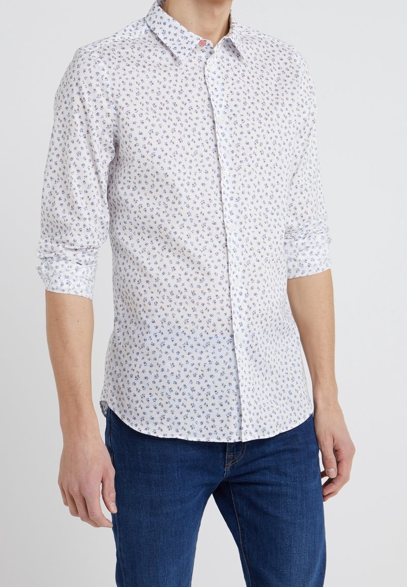 Camicia a bottoni bianca con un piccolo motivo floreale in blu e viola. Maniche lunghe arrotolate, materiale in cotone, design con colletto classico.