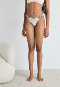 Chiloți bej tip thong cu un bandă de talie în contrast, de culoare albastră și verde. Țesătură netedă, design minimalist, se potrivesc strâns pe corp.
