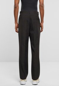 Pantalones anchos negros, hechos de una tela texturizada, con un bolsillo trasero y un pliegue en la parte delantera, combinados con zapatillas blancas.